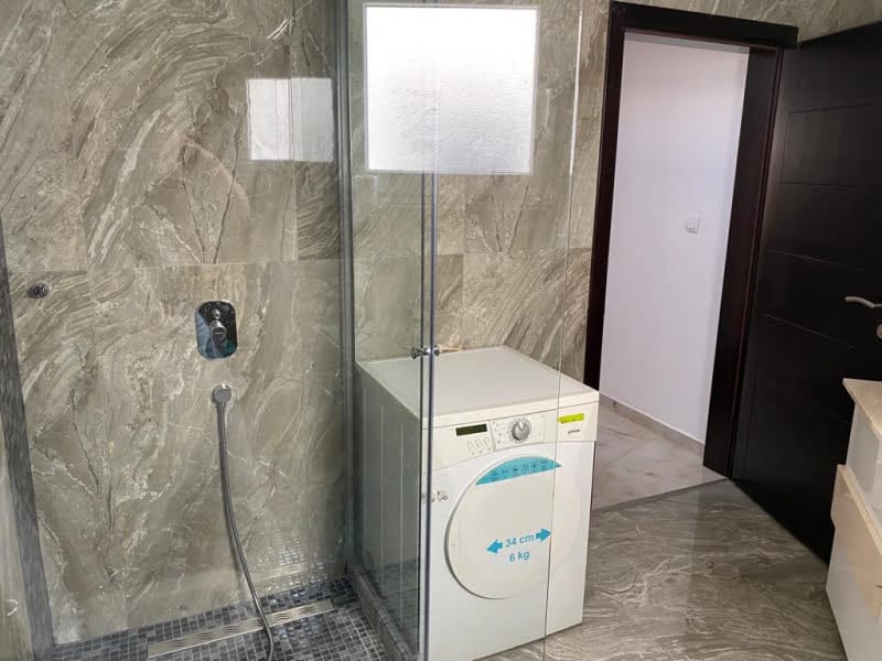 Bathroom in a house in Shushan, Montenegro: shower cabin, washing machine, and marble-look porcelain tile finish.