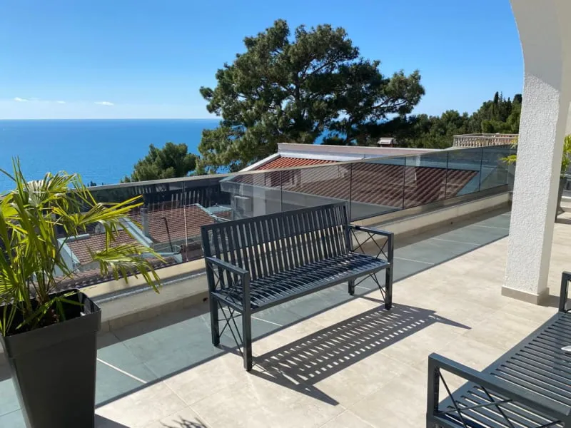 Open balcony with a metal bench and sea view, enclosed by a glass parapet wall.
