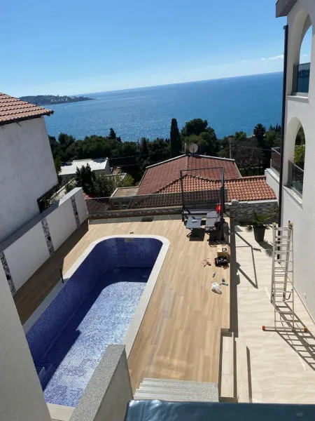 Blue tiled pool on a wooden deck terrace with sea view, ladder and construction materials visible.