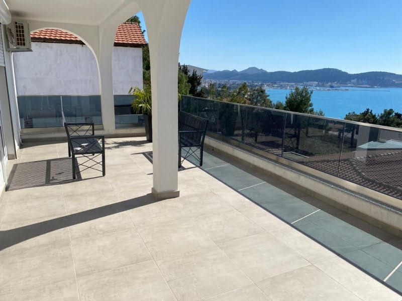 Spacious terrace with sea view in a house, Shushan, Montenegro: light tiles, wrought-iron furniture, and glass railings.