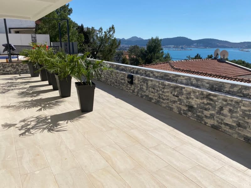 Tiled terrace with black planters containing palms and a scenic view of the sea and mountains.