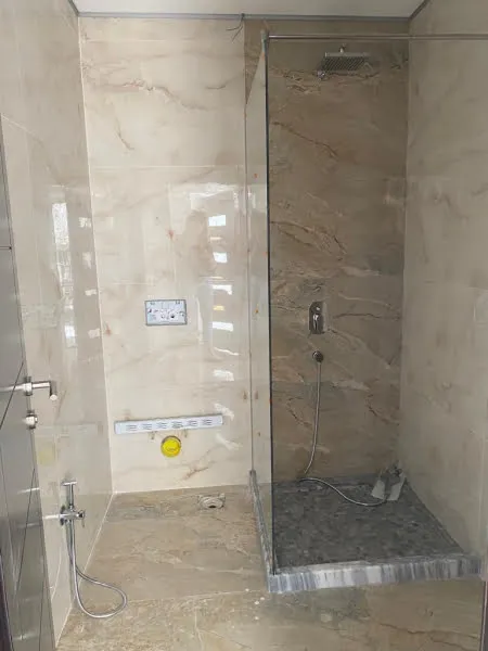 Shower area with marble tiles, glass door, and chrome fixtures. Visible plumbing pipes and unfinished construction details.