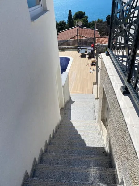 View of stone stairs leading to a terrace with a pool and sea.