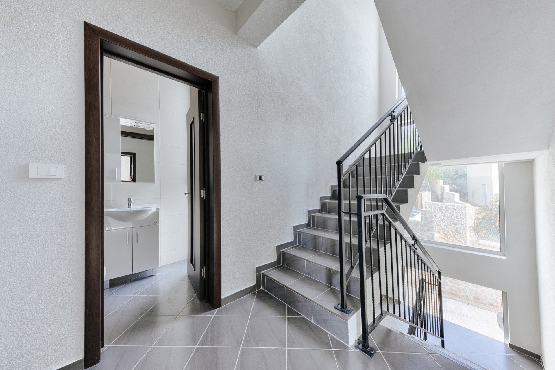 Staircase with wrought-iron railings and entrance to the bathroom in a villa in Utjeha, Montenegro: modern tile finish.