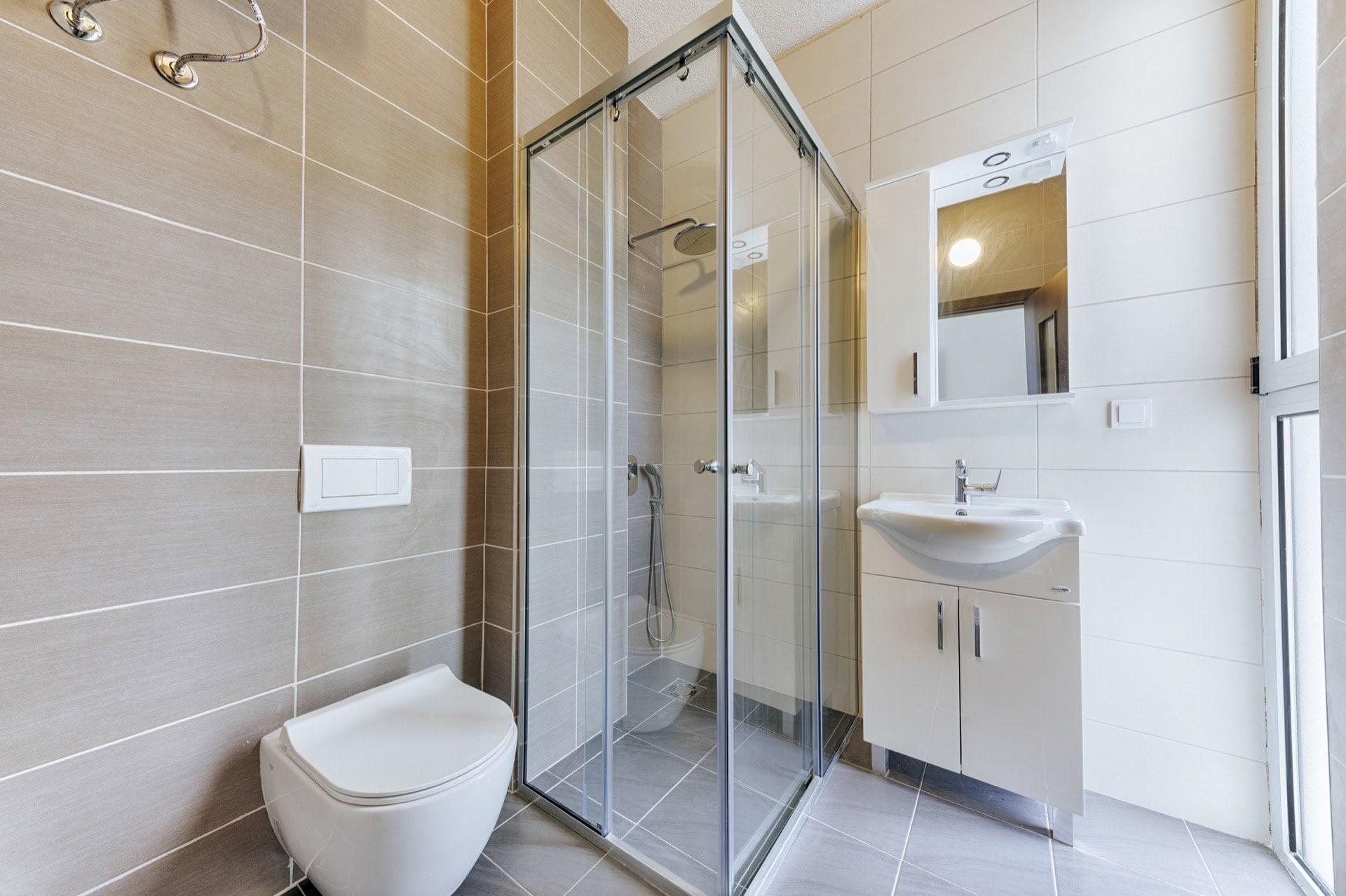 Modern bathroom with a shower cabin in a villa in Utjeha, Montenegro: tile, wall-mounted toilet, and vanity with sink.