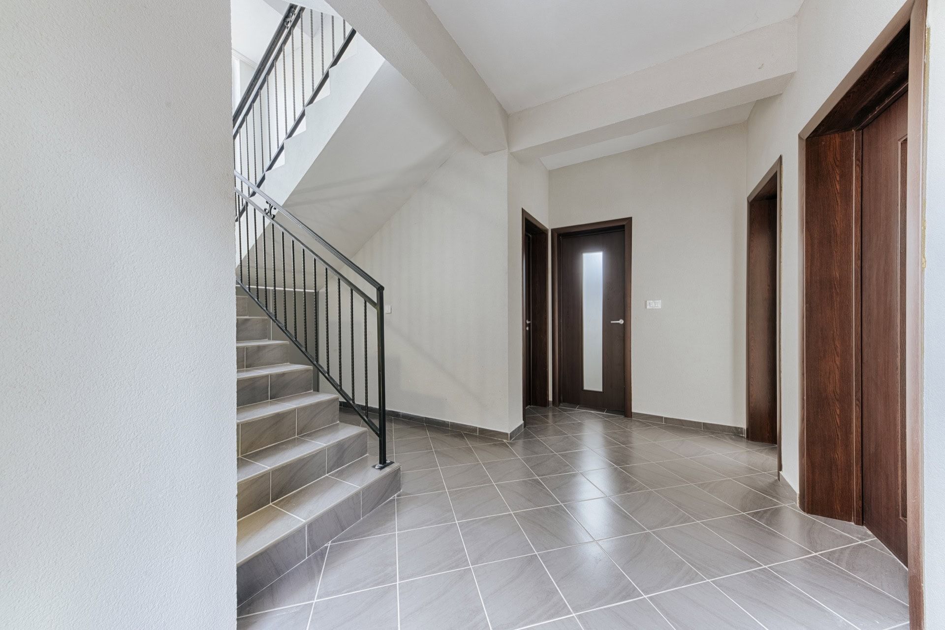 Bright hall with a staircase and dark interior doors in a villa in Utjeha, Montenegro. Modern tile finish.
