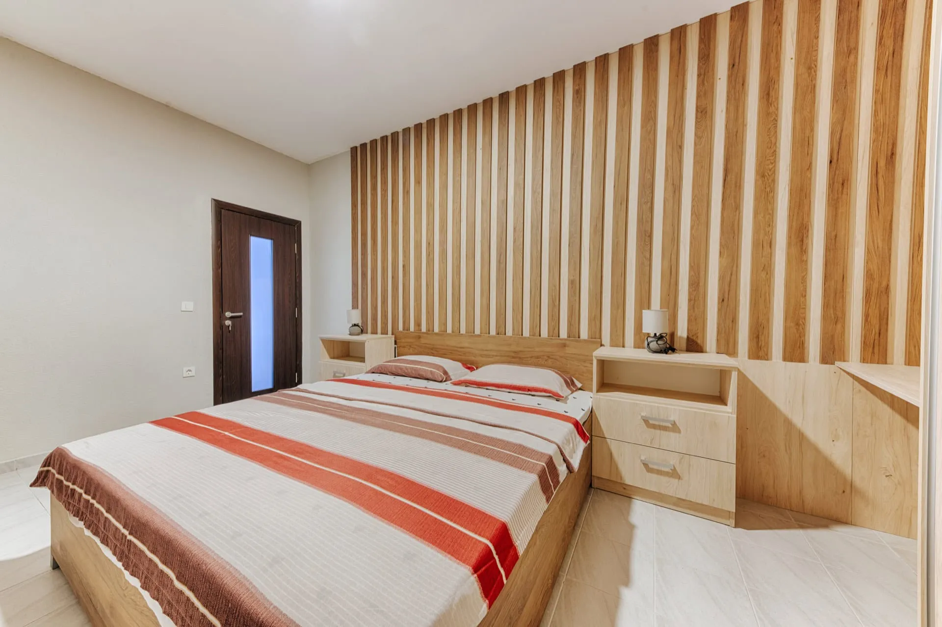 Modern bedroom featuring a vertical wood slat wall, a double bed with striped bedding, and light wooden nightstands.