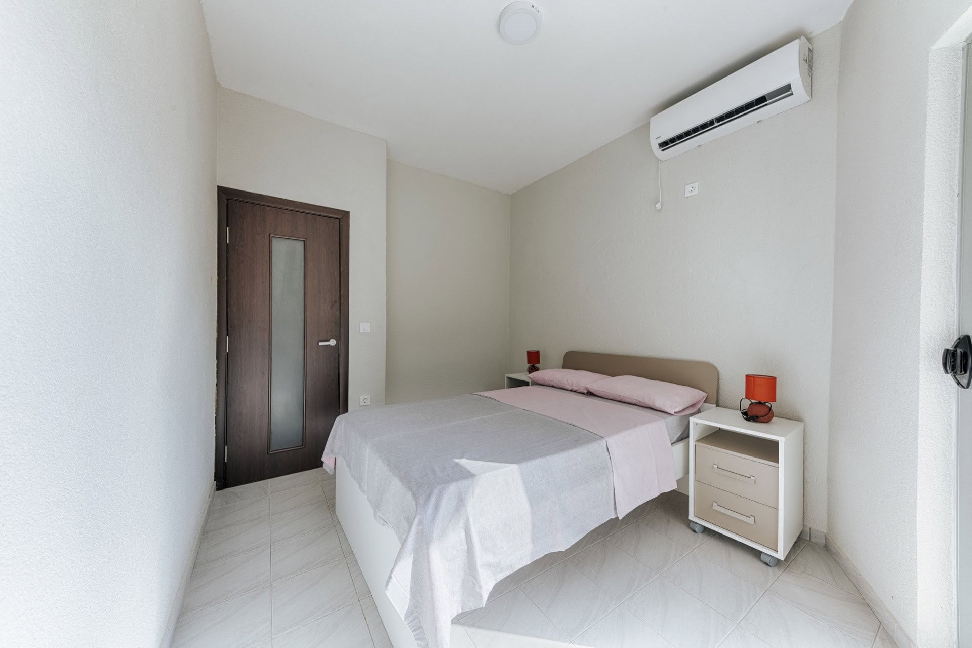 Bright bedroom with a double bed and air conditioning in a villa in Utjeha, Montenegro. Modern interior with tile flooring.