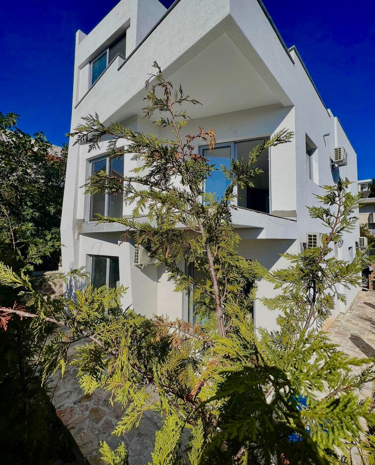 Modern white villa with panoramic windows and terraces in Utjeha, Montenegro: front view of the building and the garden.