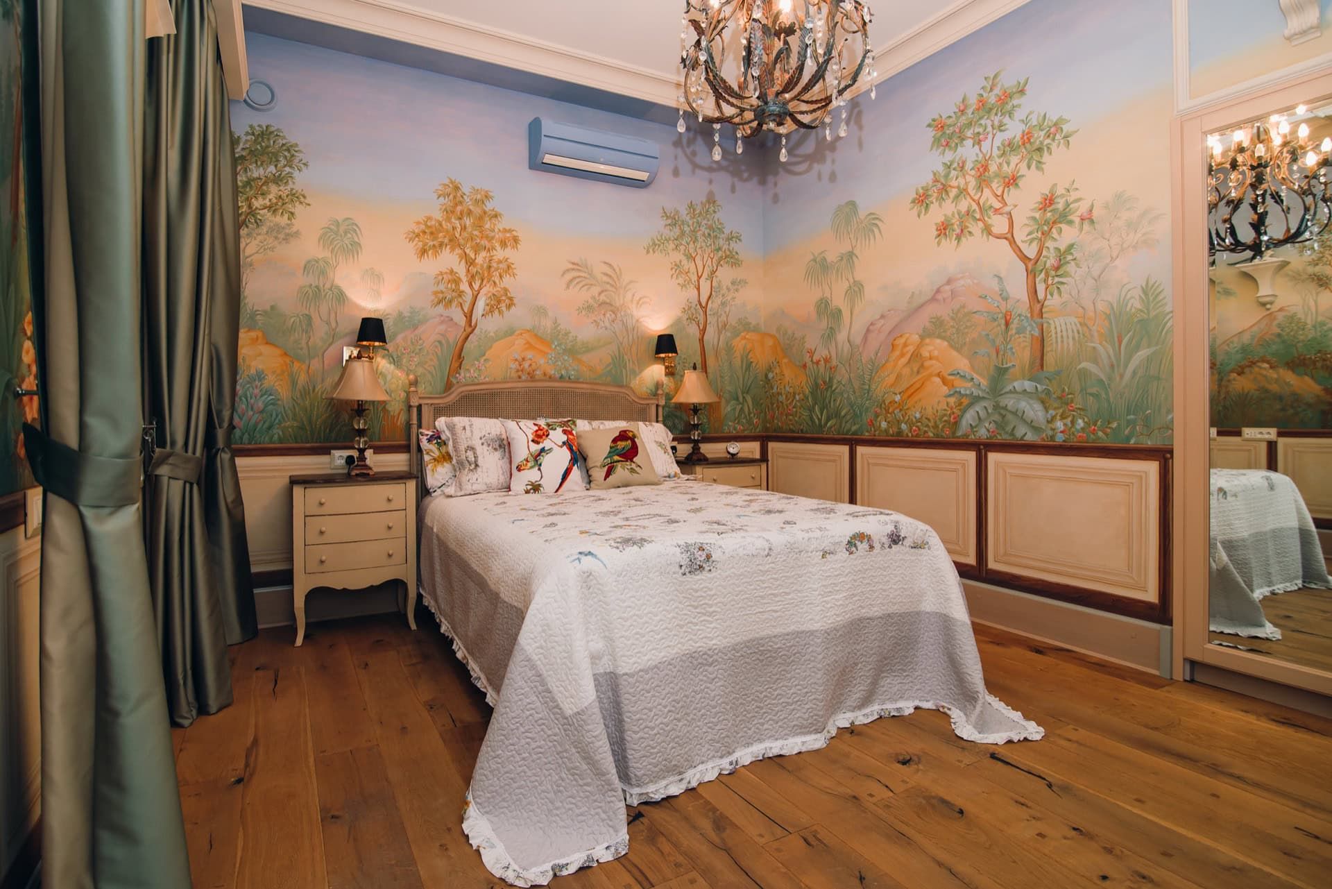 Bedroom with wall painting, a double bed, and a chandelier in a villa in Reževići, Montenegro. Wooden floor, cozy interior.