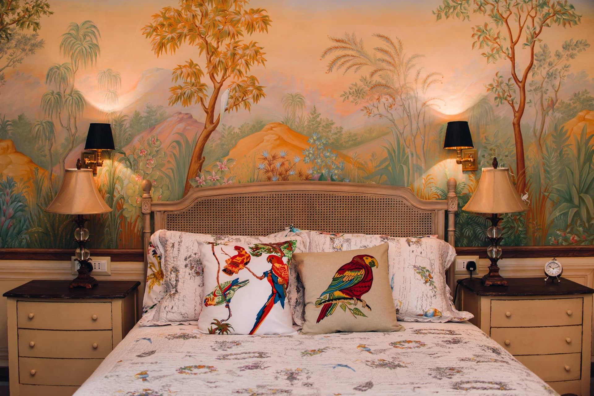 Bedroom in a villa in Rezevici, Montenegro: a bed with a woven headboard, custom landscape wallpaper, and parrot decor.