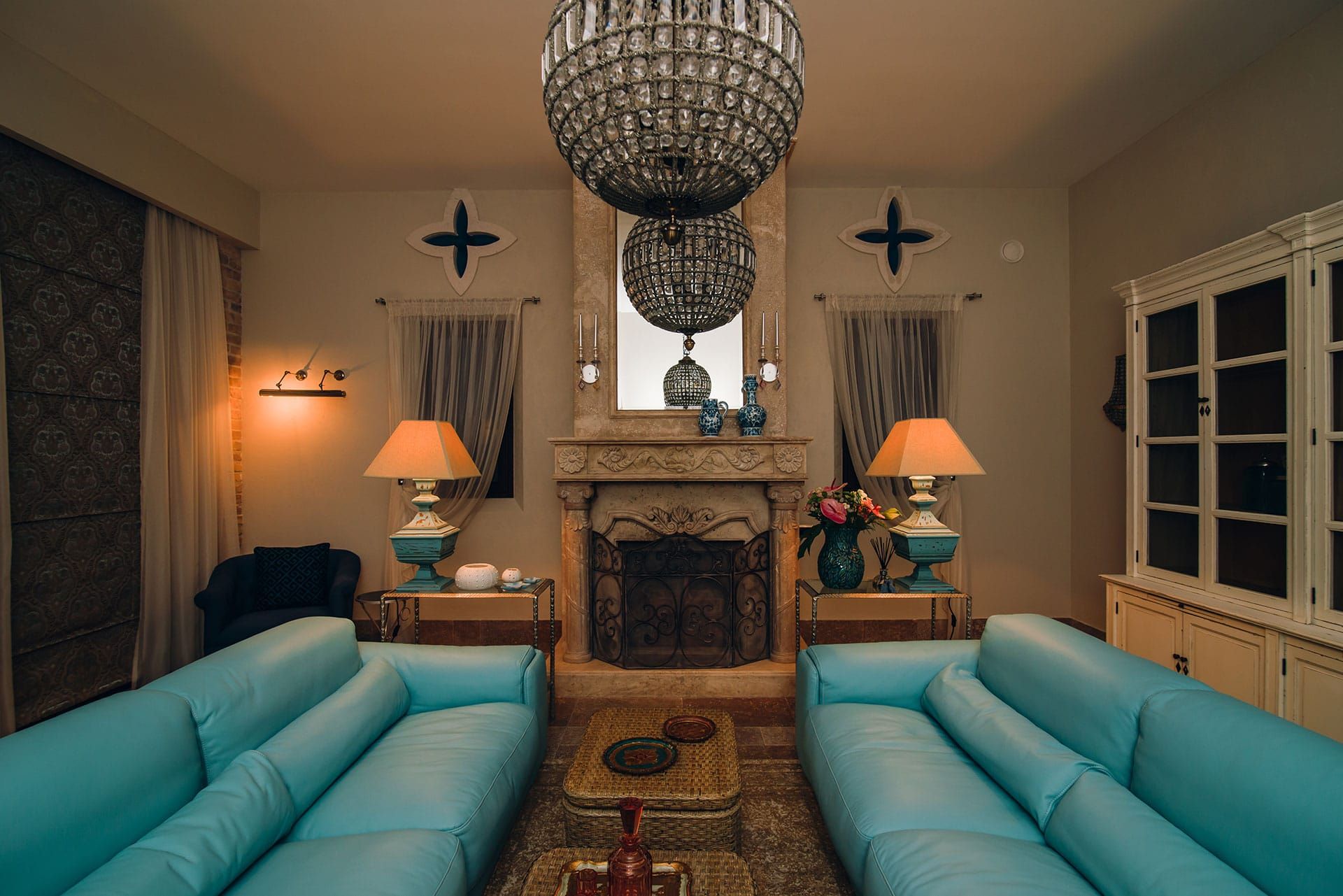 Villa living room in Reževići, Montenegro: fireplace, crystal chandeliers, turquoise leather sofas, and a classic interior.