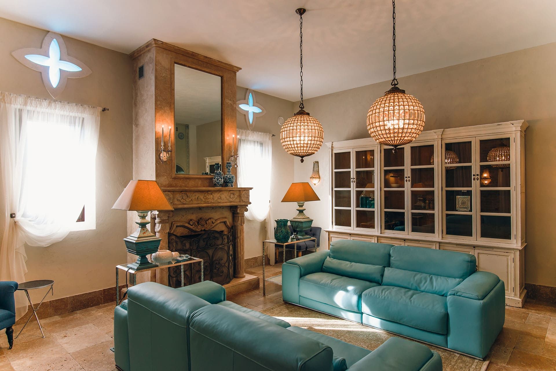Villa living room in Reževići, Montenegro: turquoise leather sofas, stone fireplace, vintage cabinet, and chandeliers.