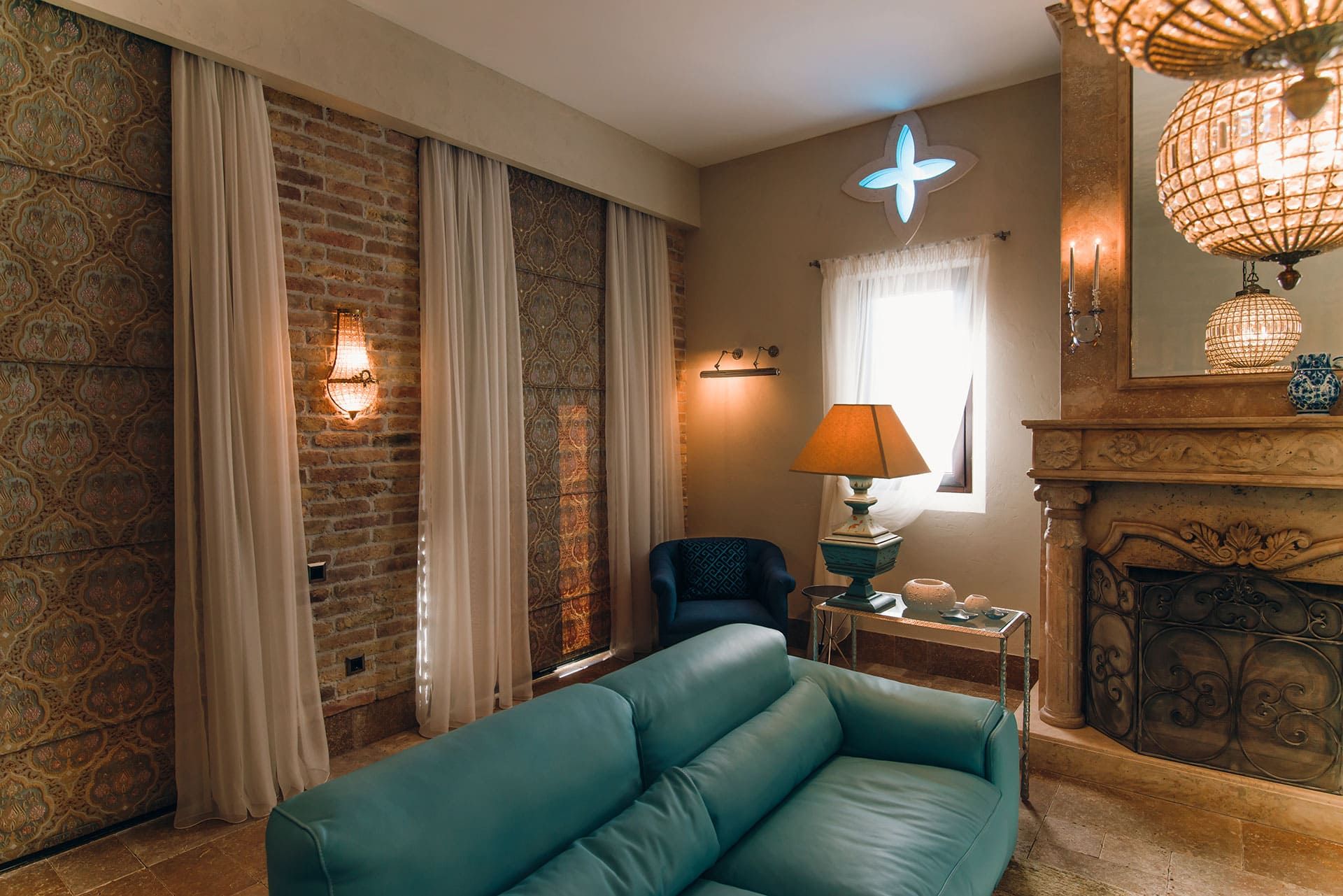 Villa living room in Reževići, Montenegro: leather sofa, stone fireplace, brick wall, and crystal chandeliers.