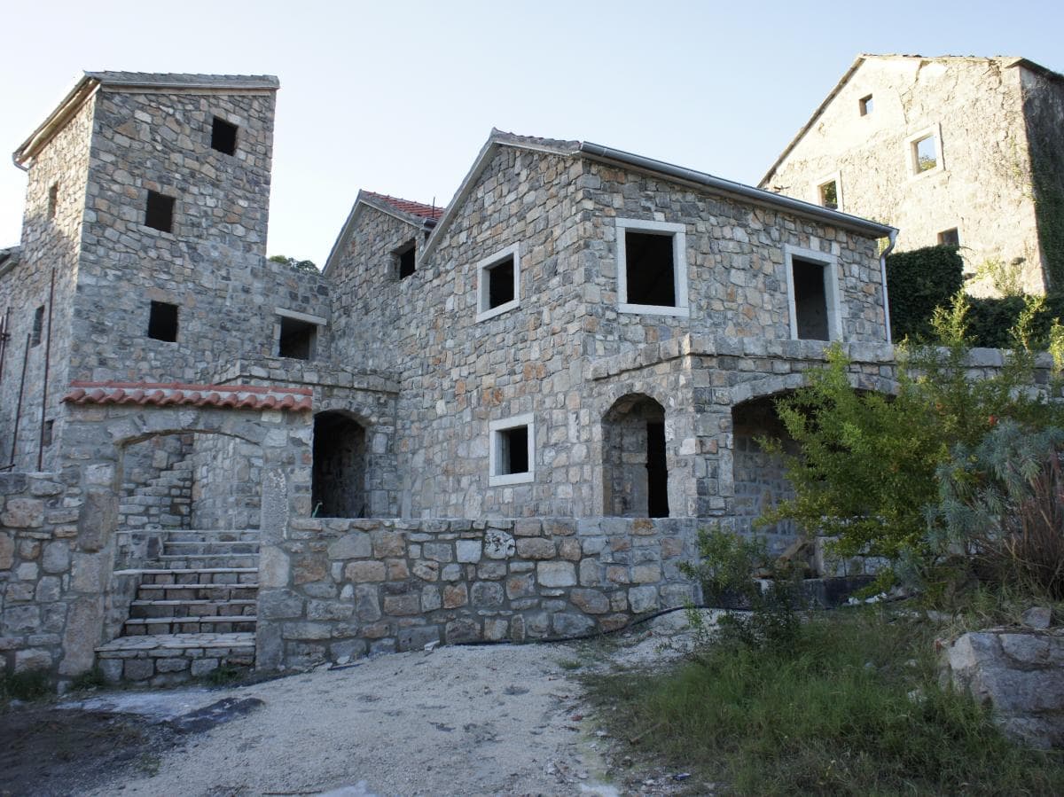 Exterior view of an old stone building featuring arched openings, a stone staircase, and empty window frames under a clear sky.