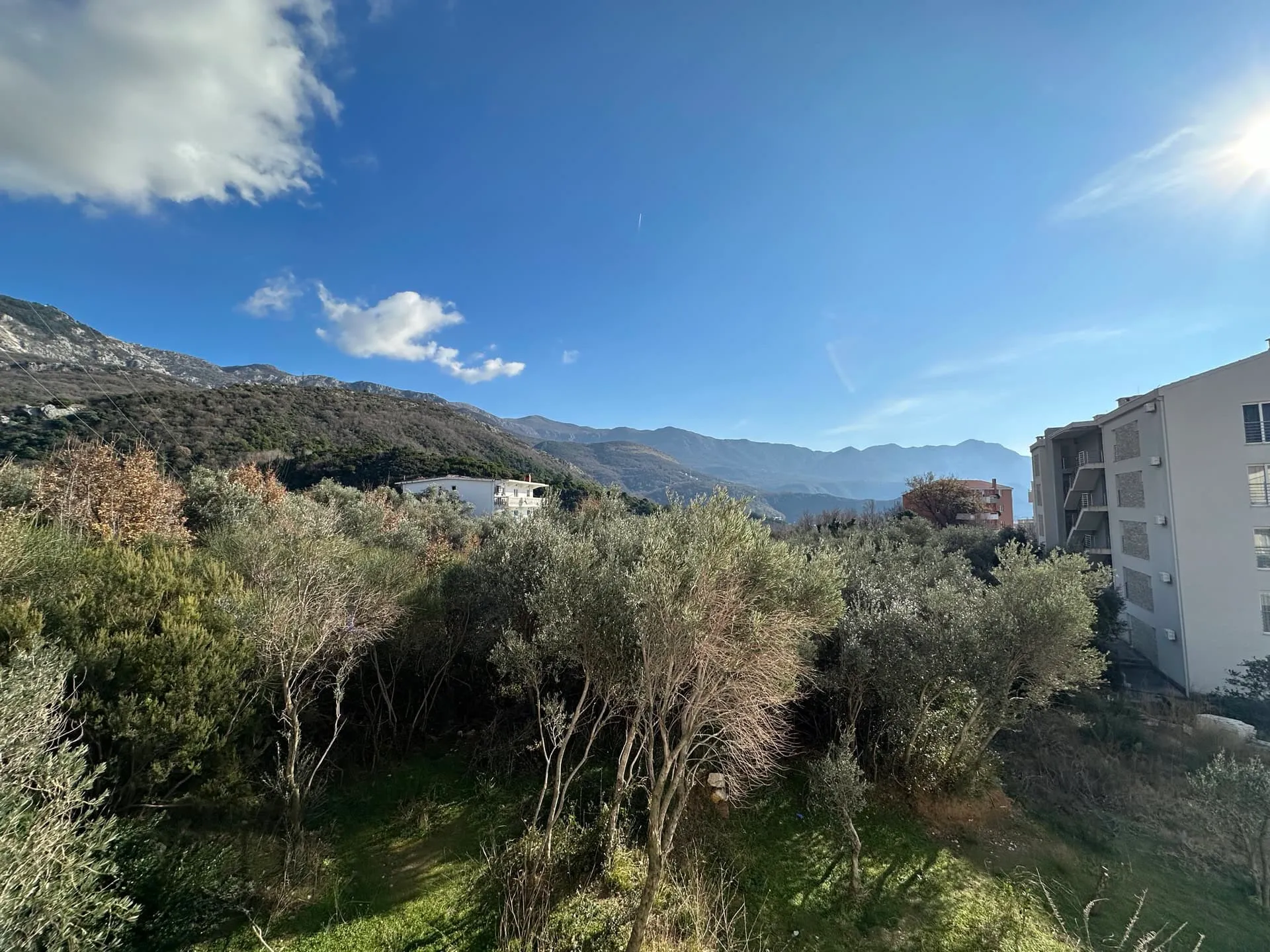 Scenic exterior view of mountains and dense vegetation with residential buildings under a clear blue sky.