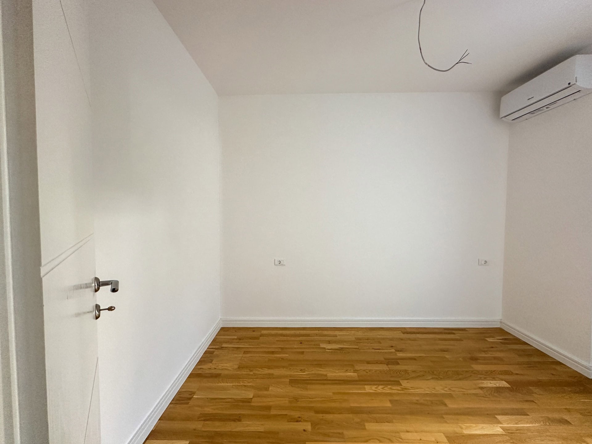 Bright bedroom with parquet flooring and air conditioning in a new apartment in Bečići, Montenegro. Empty room with white walls.