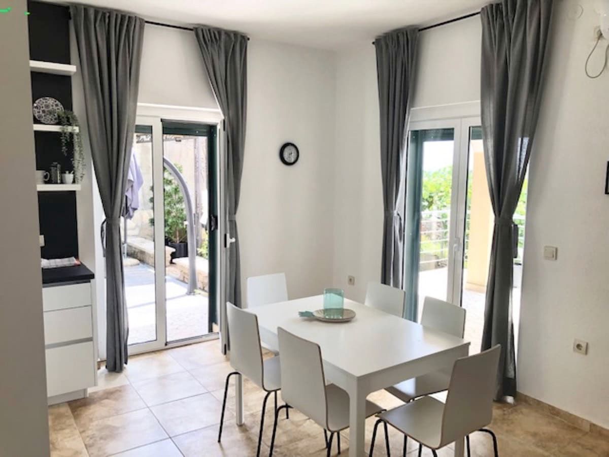 Bright living room with dining area in a villa in Krimovica, Montenegro: white furniture, panoramic windows, and access to the terrace.