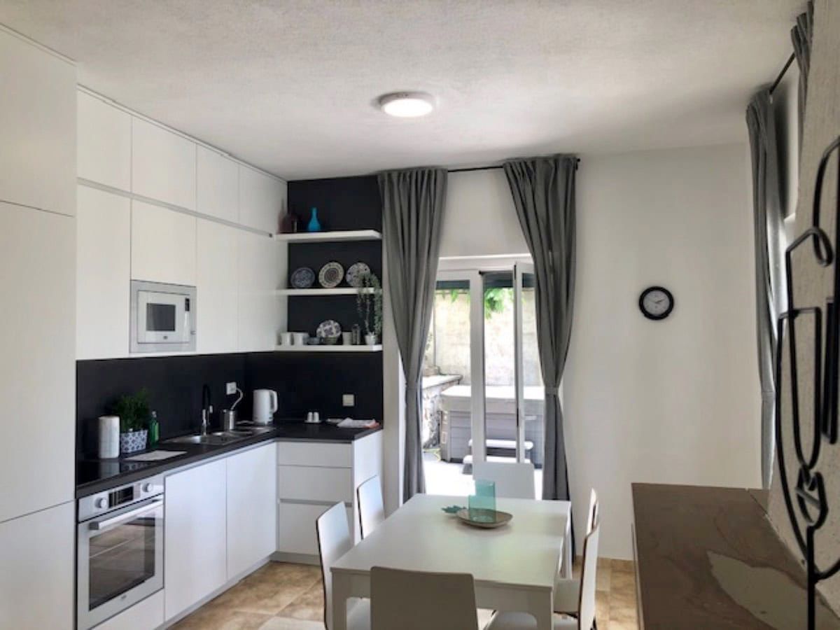 Modern kitchen-dining room with white cabinetry in a villa in Krimovica, Montenegro, with access to the terrace.