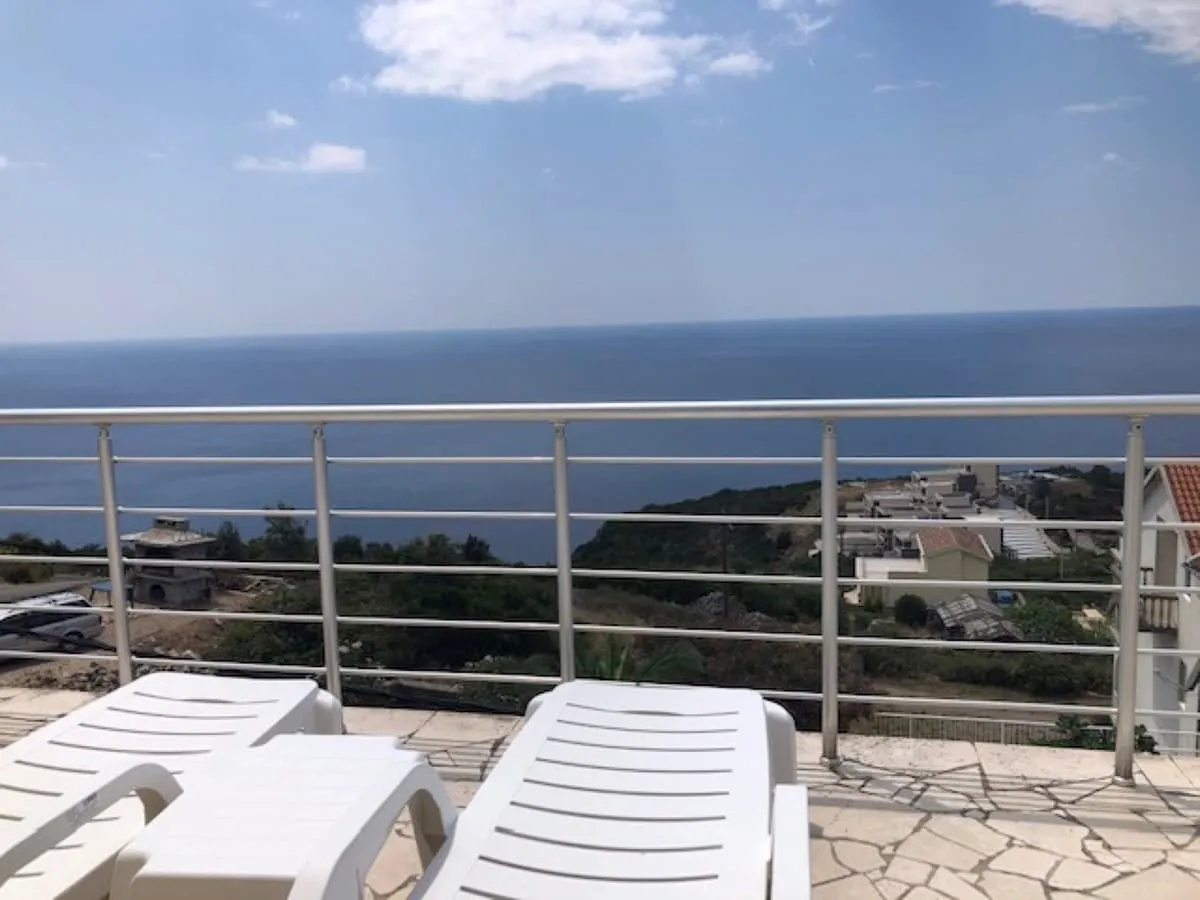 Terrace with white sun loungers and metal railing overlooking the sea and coast.