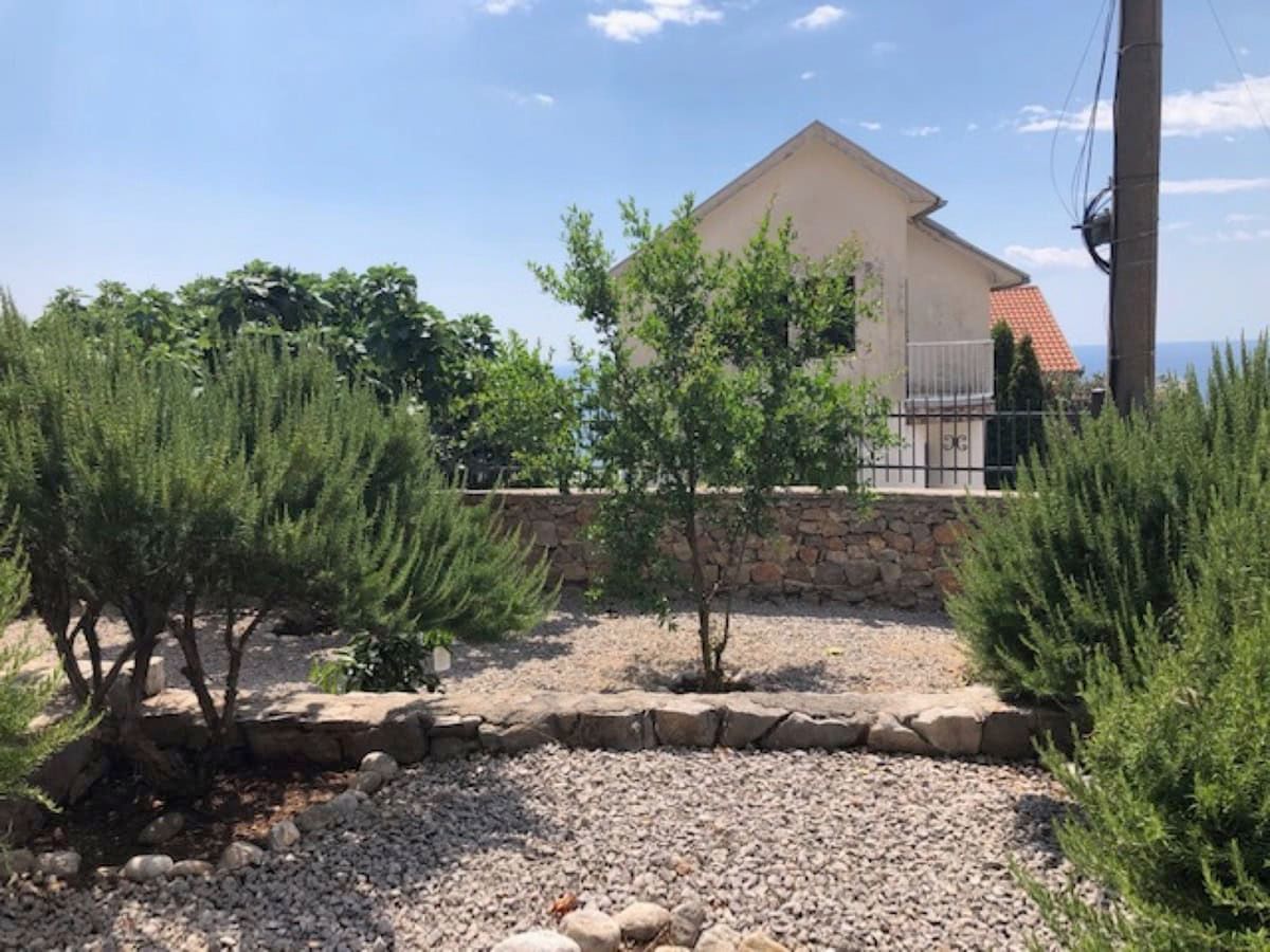 Well-kept garden with gravel and green shrubs by a villa in Krimovica, Montenegro, view of the house and the sea.