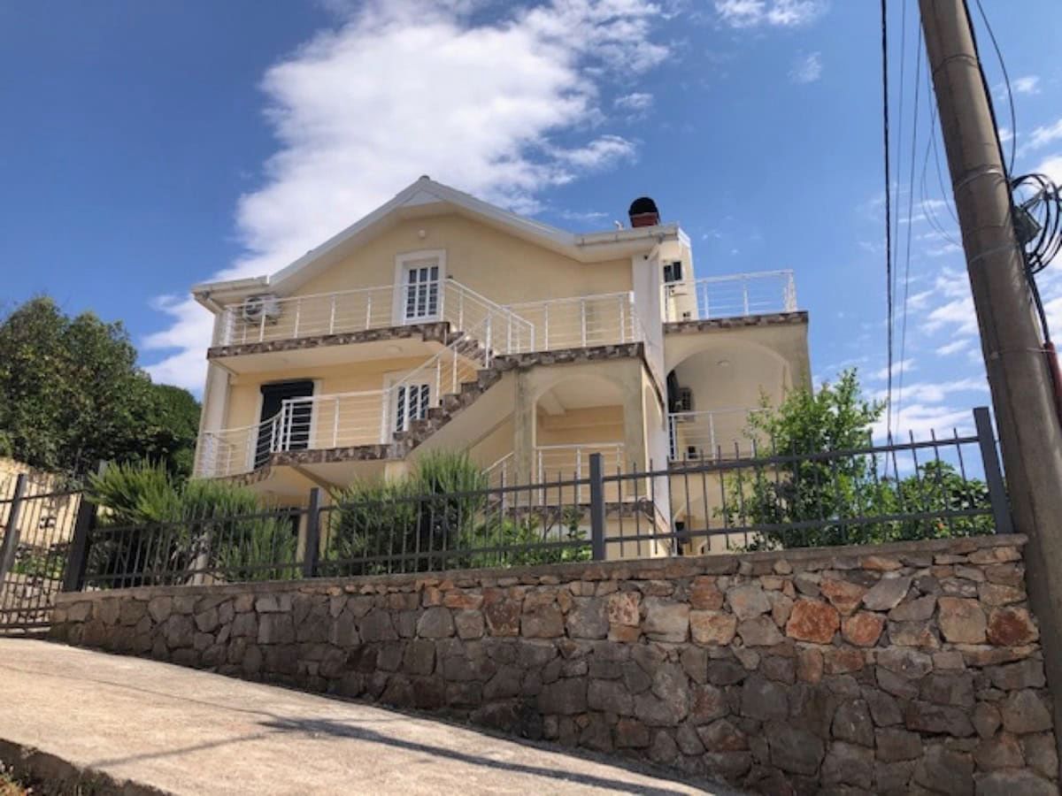 Two-story villa in Krimovica, Montenegro: light facade, open terraces with railings, and a stone perimeter fence.