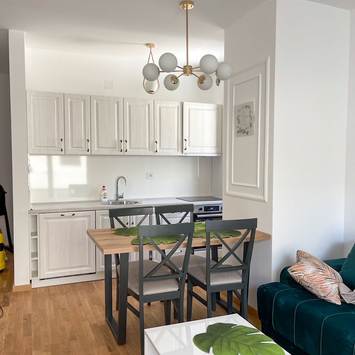 Modern kitchen-living room in an apartment in Bečići, Montenegro: light-colored cabinetry, dining area, and an emerald sofa.