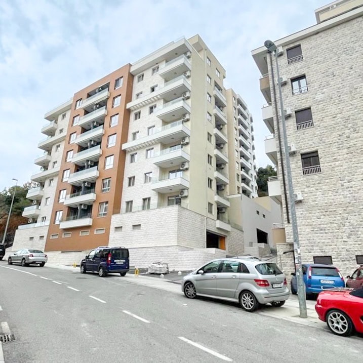 Modern residential complex with balconies in Bečići, Montenegro: view of a multi-story building with parking in front of the facade.