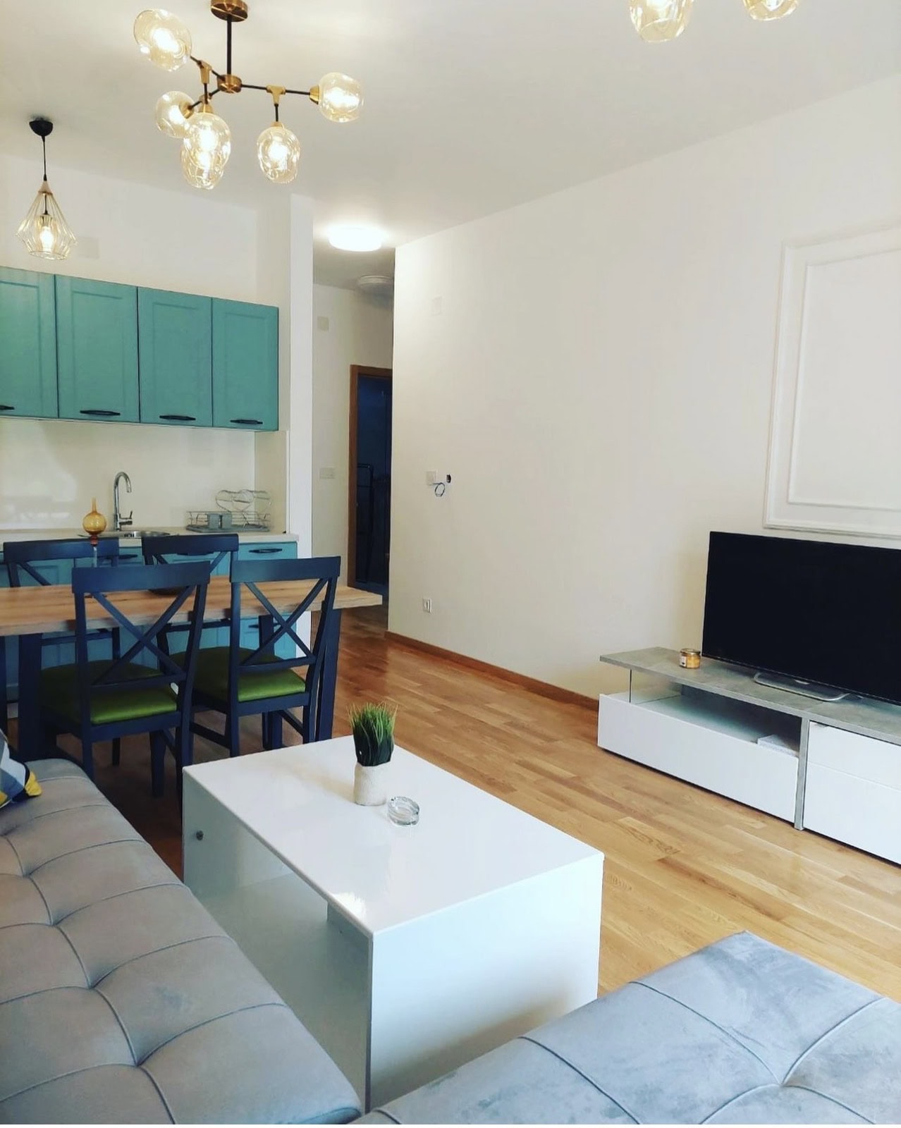 Modern living room with kitchen in an apartment in Bečići, Montenegro: turquoise kitchen set, dining area, and TV area.