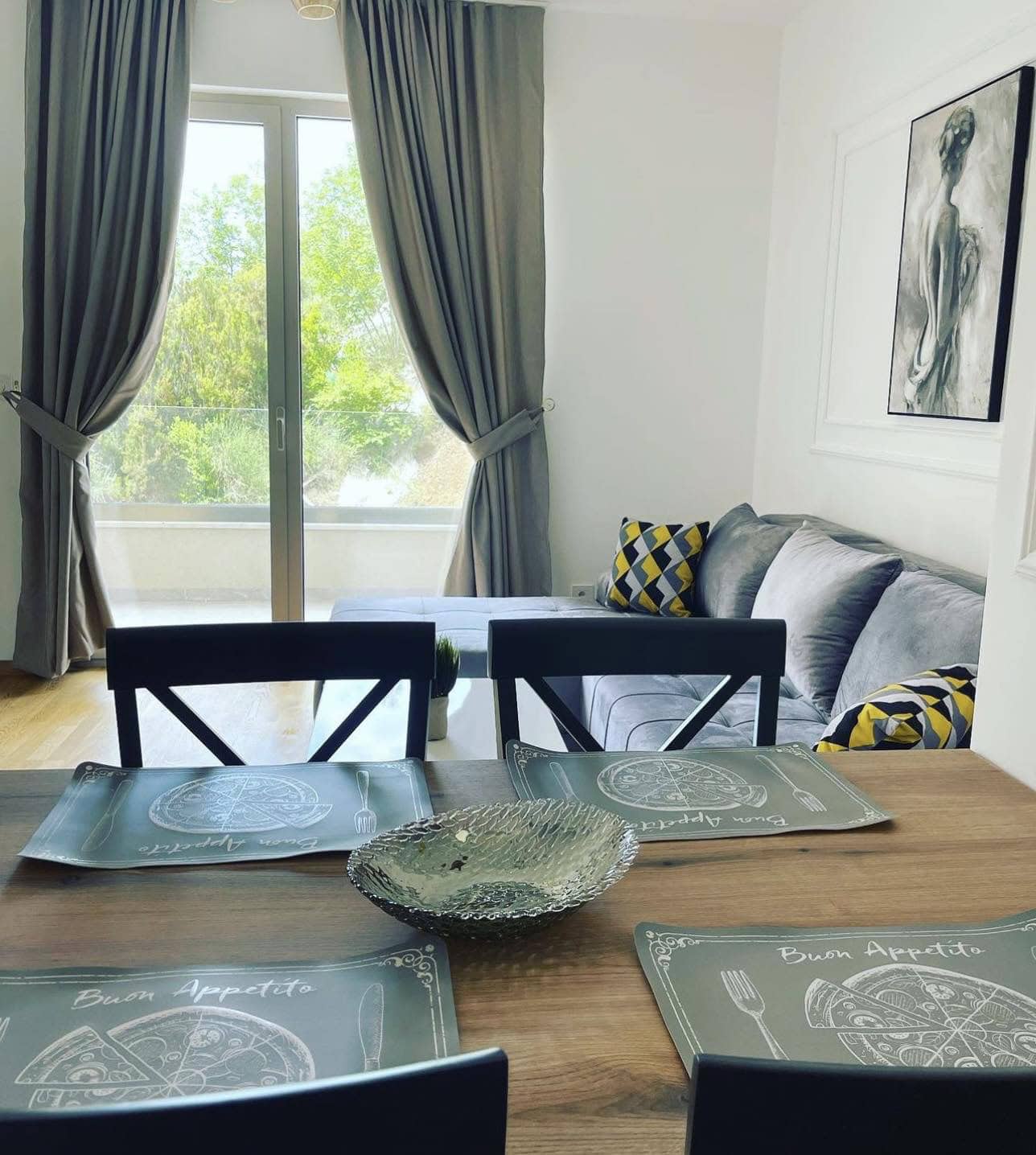 Living room with dining area in an apartment in Becici, Montenegro: modern furniture, panoramic window, and a view of greenery.