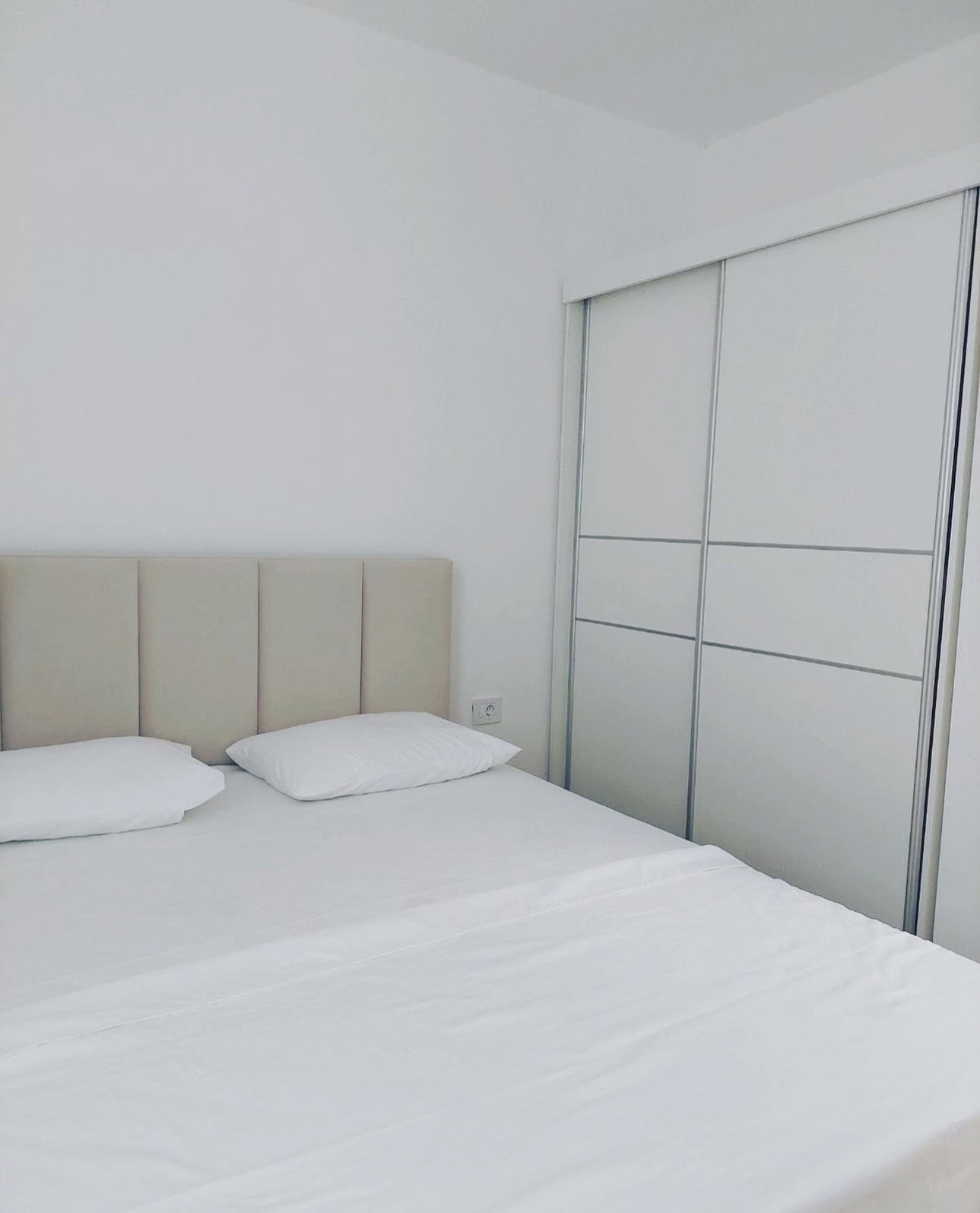 Bright bedroom in an apartment in Bečići, Montenegro: a double bed with a soft headboard and a white sliding wardrobe.
