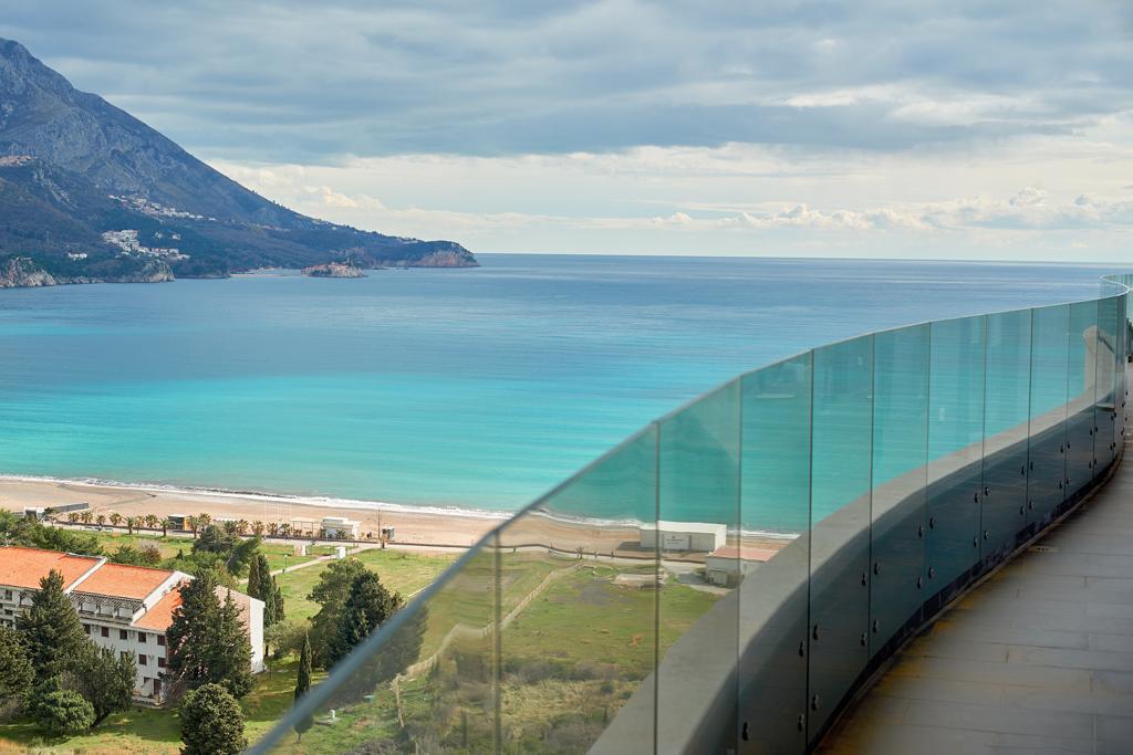 Panoramic view of the sea and beach from the apartment balcony in Bečići, Montenegro, with a glass railing and terrace.