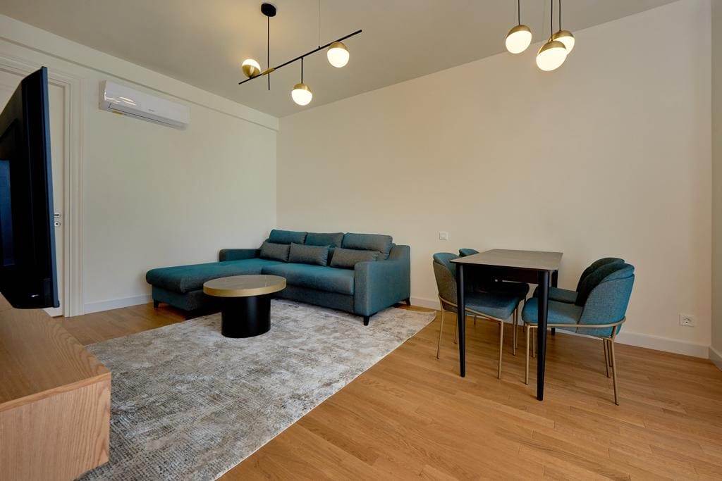 Modern living room with a blue sofa and dining area in an apartment in Bečići, Montenegro. Bright interior with parquet flooring.