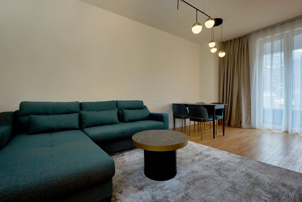 Modern living room with a blue sofa and dining area in an apartment in Bečići, Montenegro, with access to the balcony.
