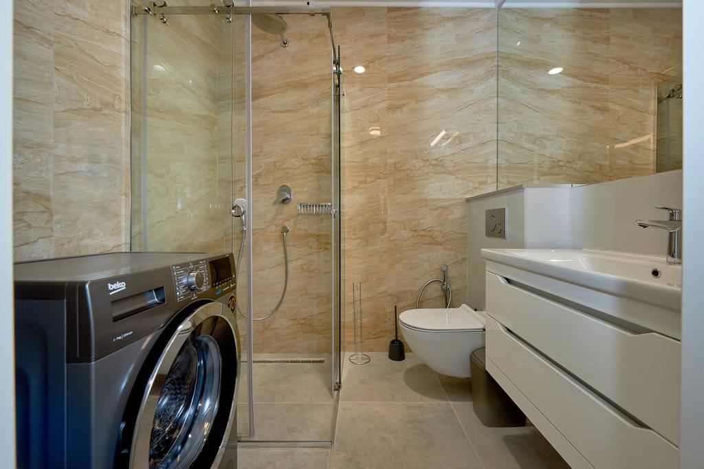 Modern bathroom in an apartment in Bečići, Montenegro: shower cabin, washing machine, and white furniture.