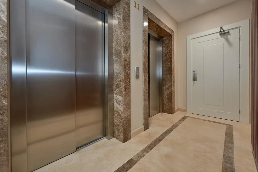 Elevator lobby featuring two stainless steel elevator doors, brown marble wall trim, and a white door on the 11th floor.