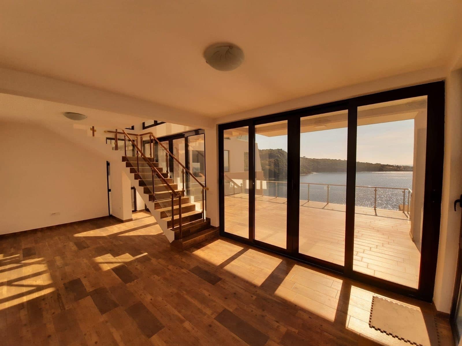 Living room of a villa in Kruče, Montenegro: panoramic windows, sea view, terrace, and staircase with wooden steps.