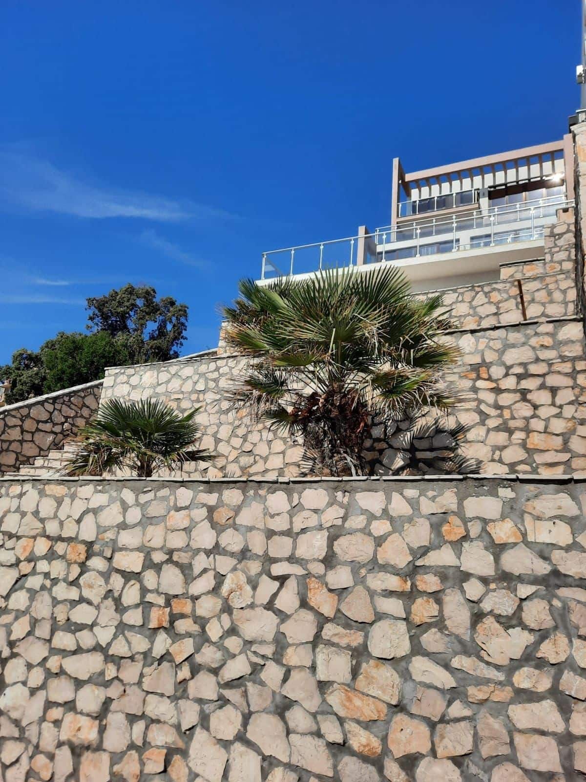 Modern villa with a terrace and stone facade in Kruče, Montenegro, against a blue sky.