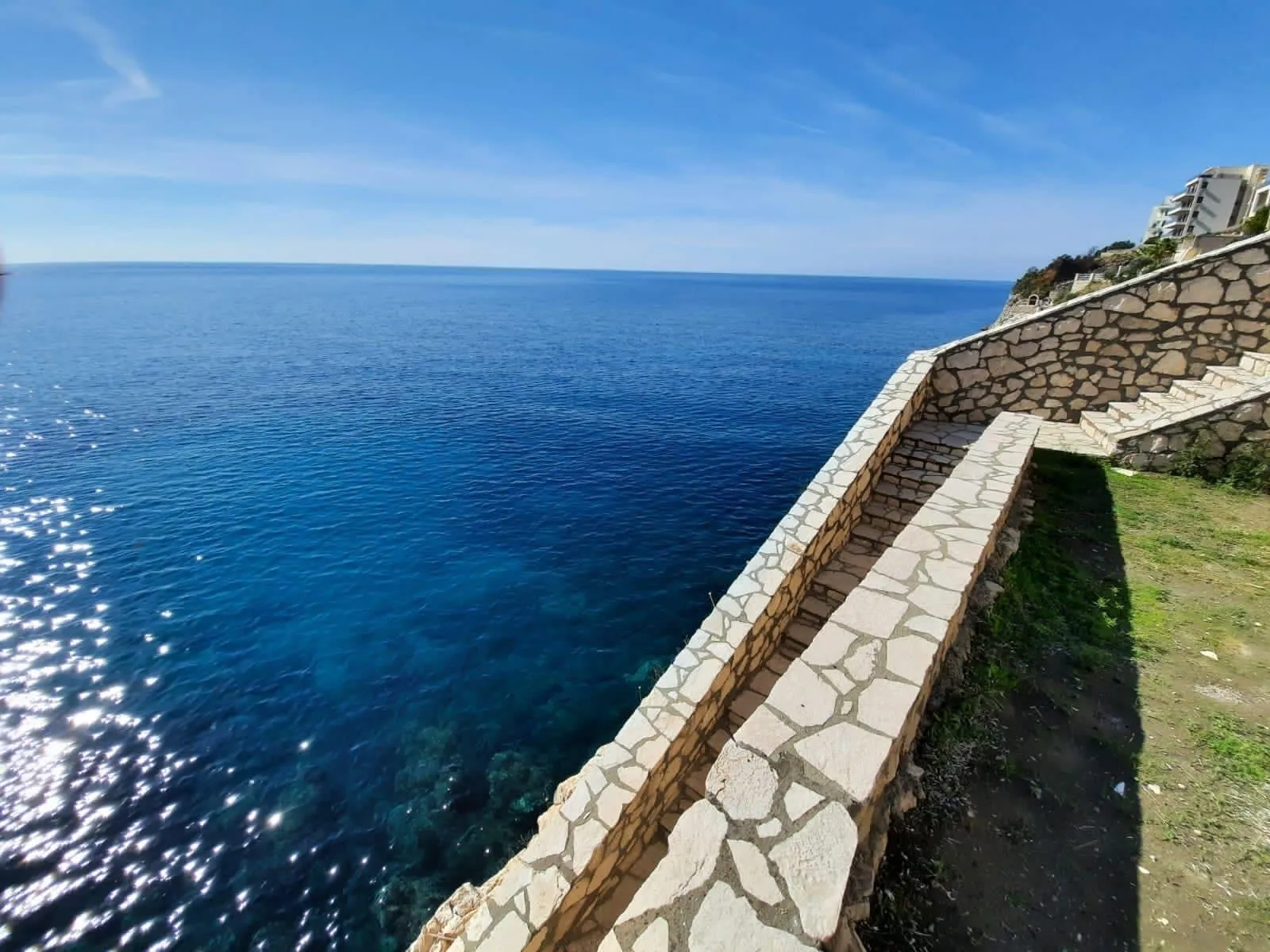 Stone wall and steps along the coastline overlooking deep blue sea under clear sky.
