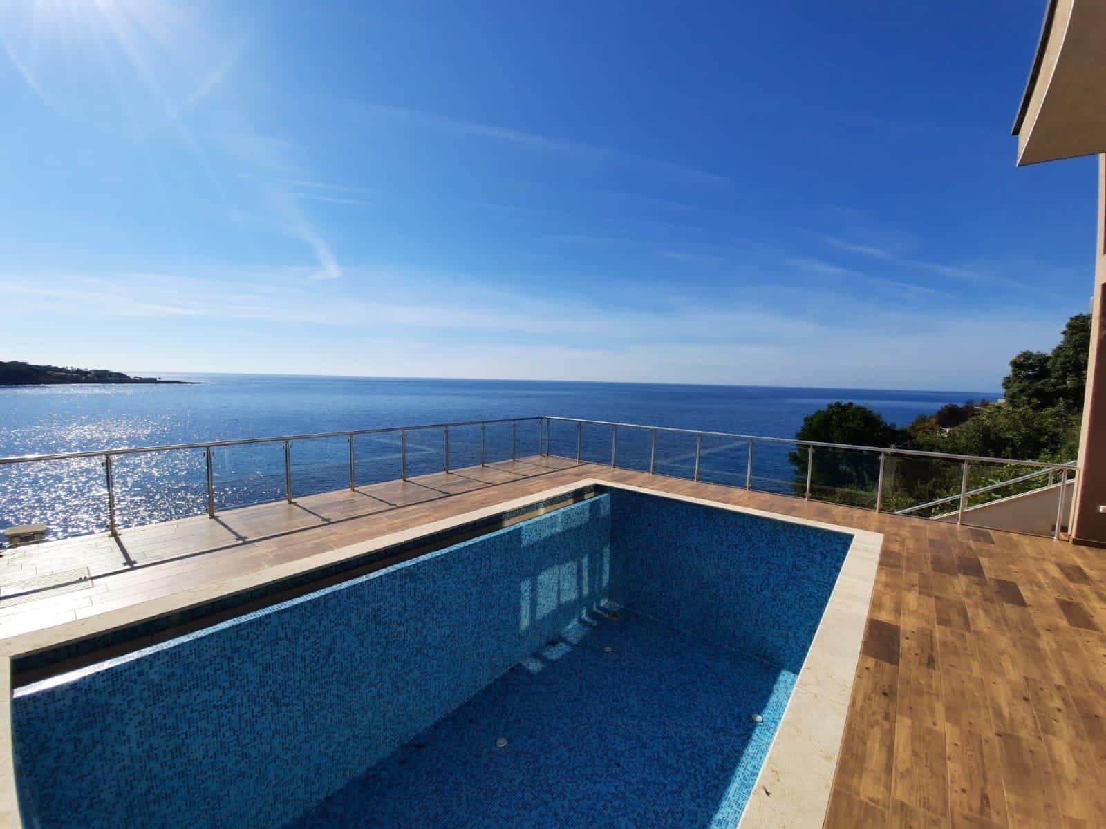 Outdoor swimming pool on a villa terrace in Dobra Voda, Montenegro, with a panoramic view of the Adriatic Sea and the mountains.