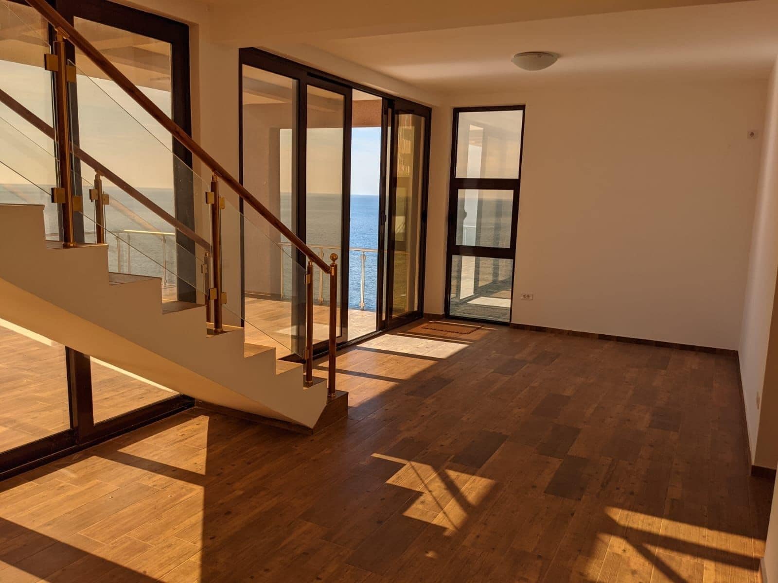 Living room with a panoramic sea view in a villa, Dobra Voda, Montenegro: staircase, wooden floor, glass doors.