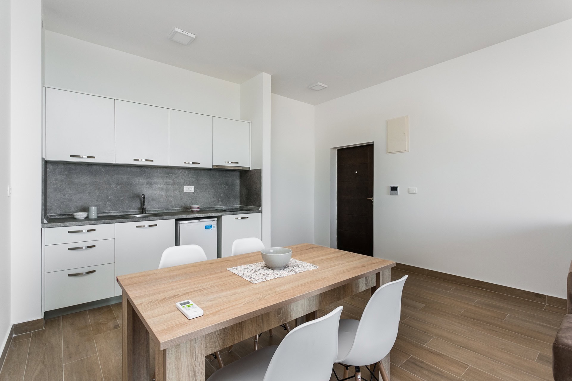 Modern kitchen-dining room in an apartment, Budva, Montenegro: white fronts, wooden table and chairs, stylish interior.