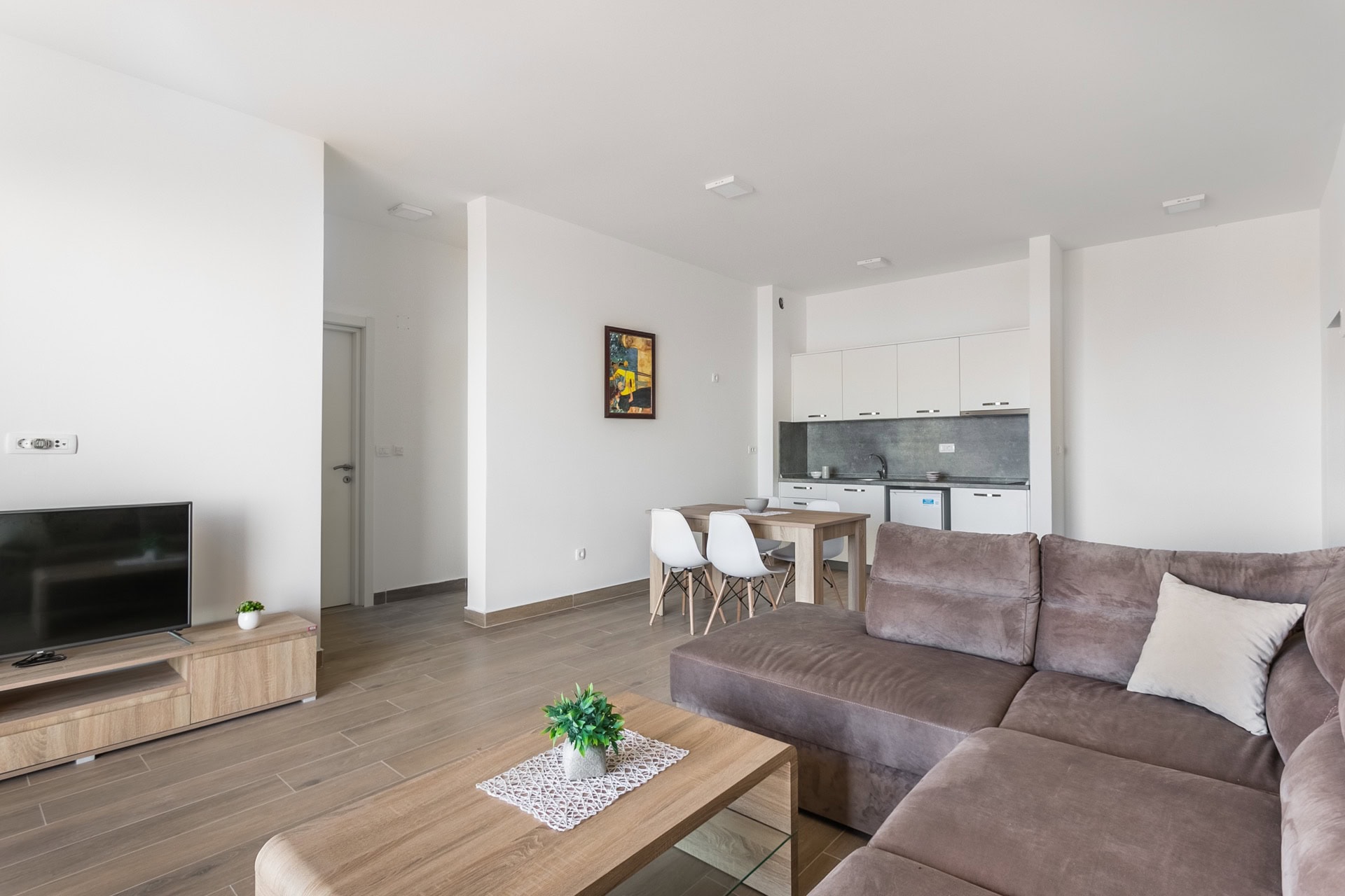 Modern living room with kitchen in an apartment in Budva, Montenegro: brown sofa, dining area, and light finishes.