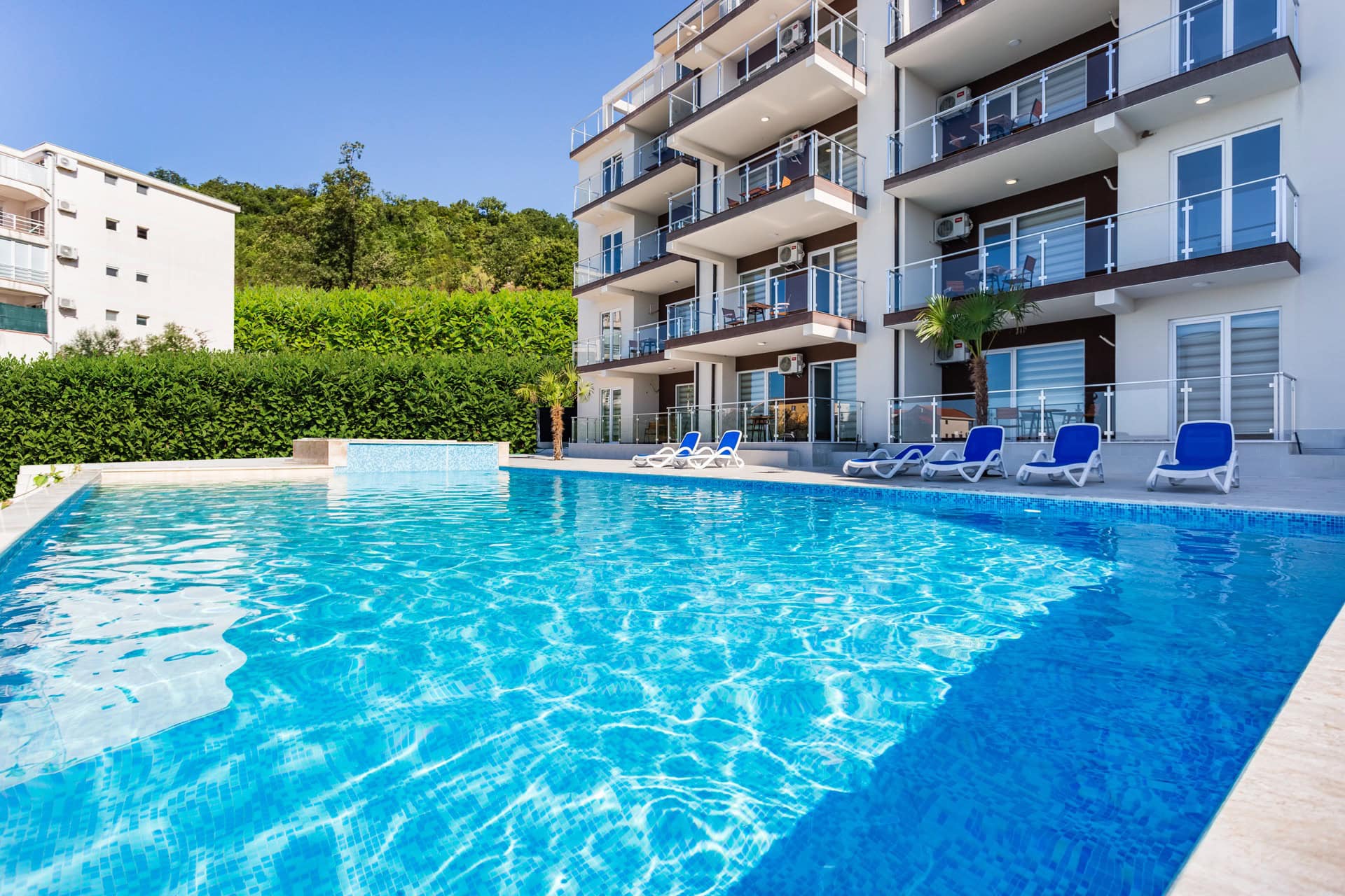 Modern residential complex with a pool and sun loungers in Seoce, Budva, Montenegro. View of apartments with terraces.