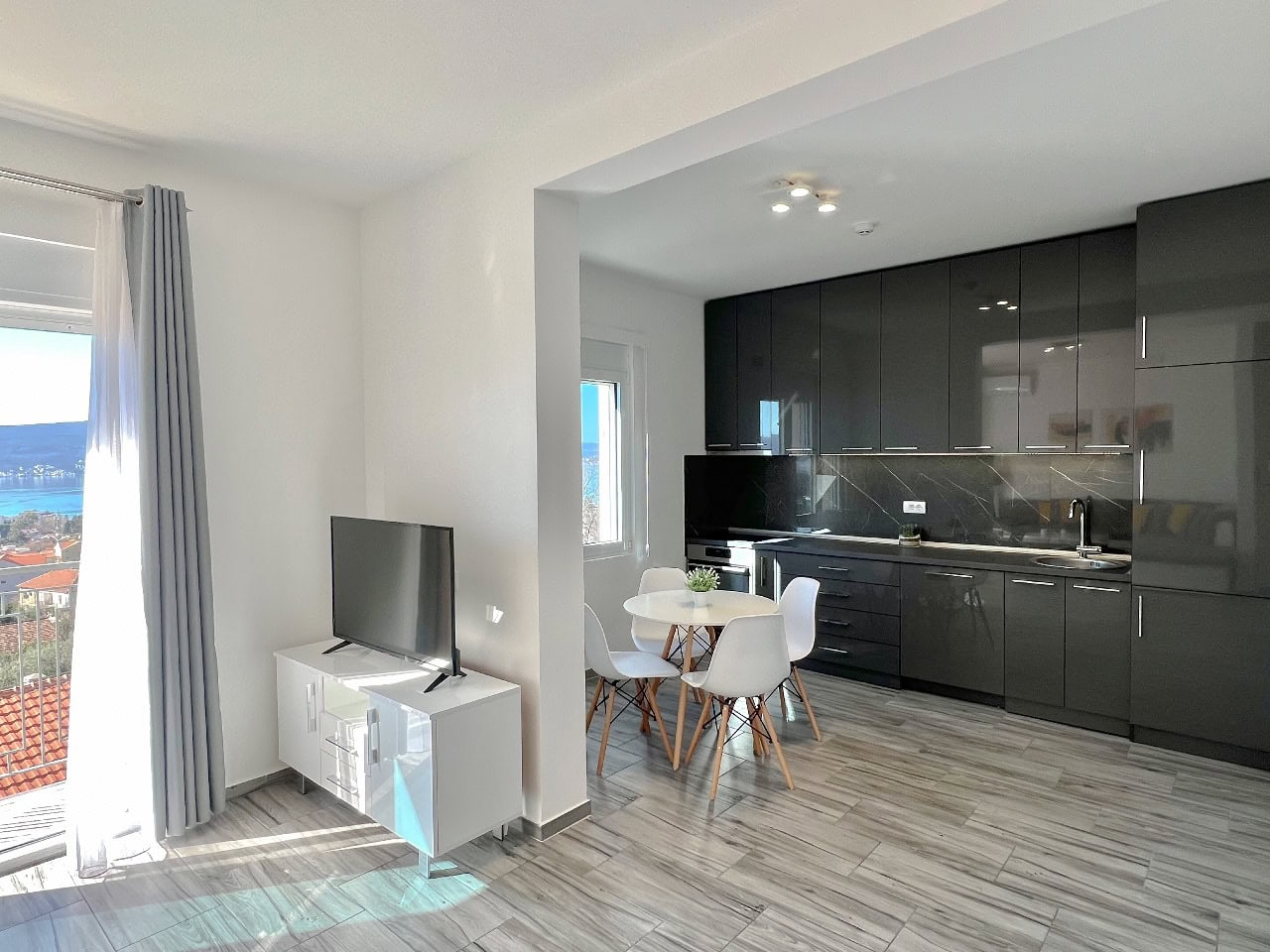 Modern living room with kitchen in an apartment in Tivat, Montenegro: dark cabinetry, dining area, and sea view.