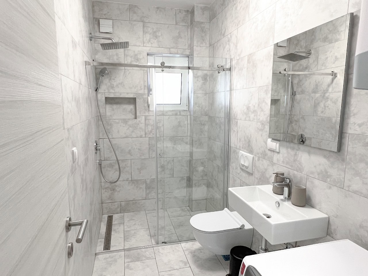 Modern bathroom with a shower cabin in an apartment, Tivat, Montenegro: light tiles, wall-hung toilet and sink.
