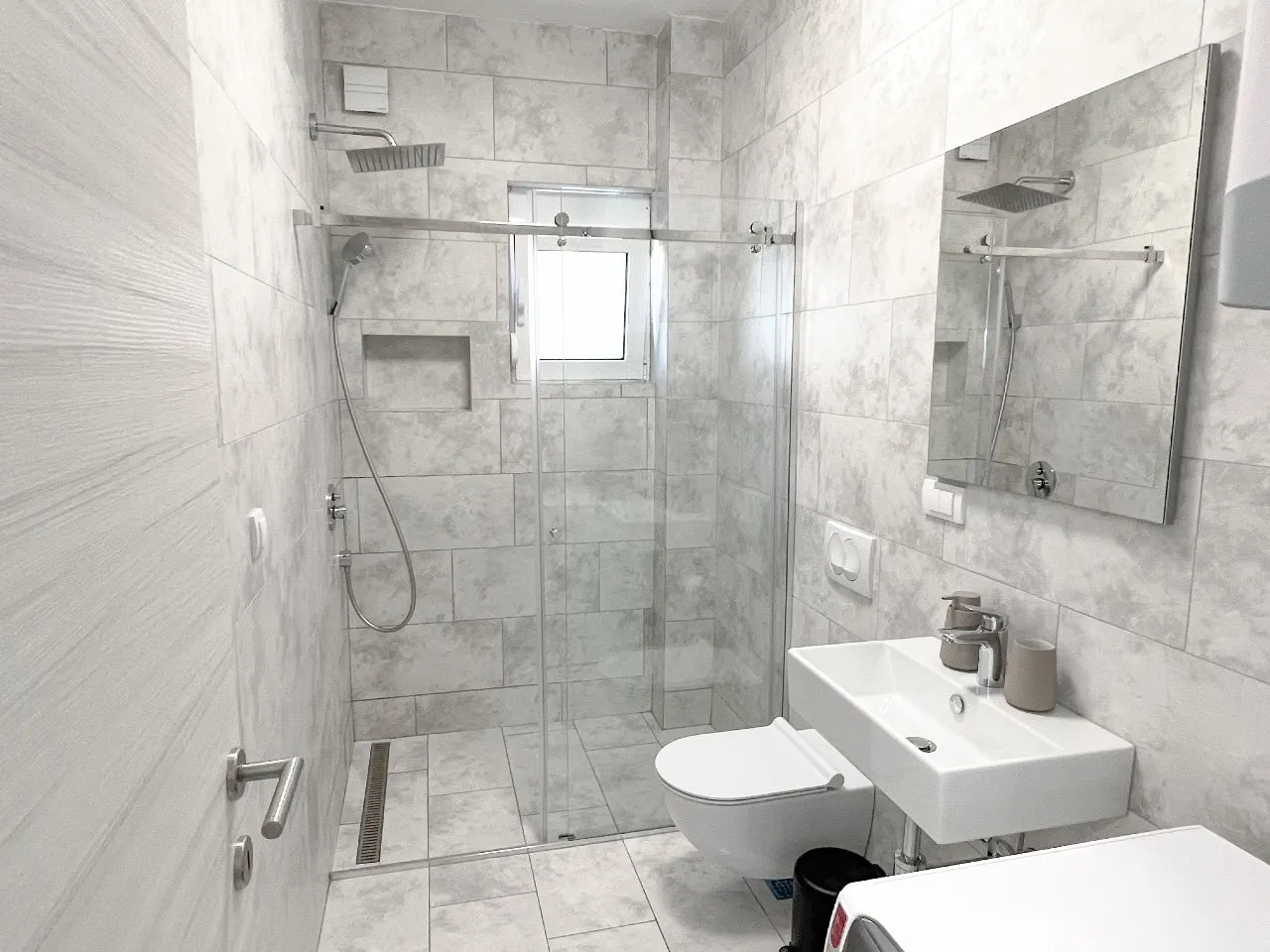 Modern bathroom featuring a glass shower enclosure, wall-mounted toilet, and white sink.