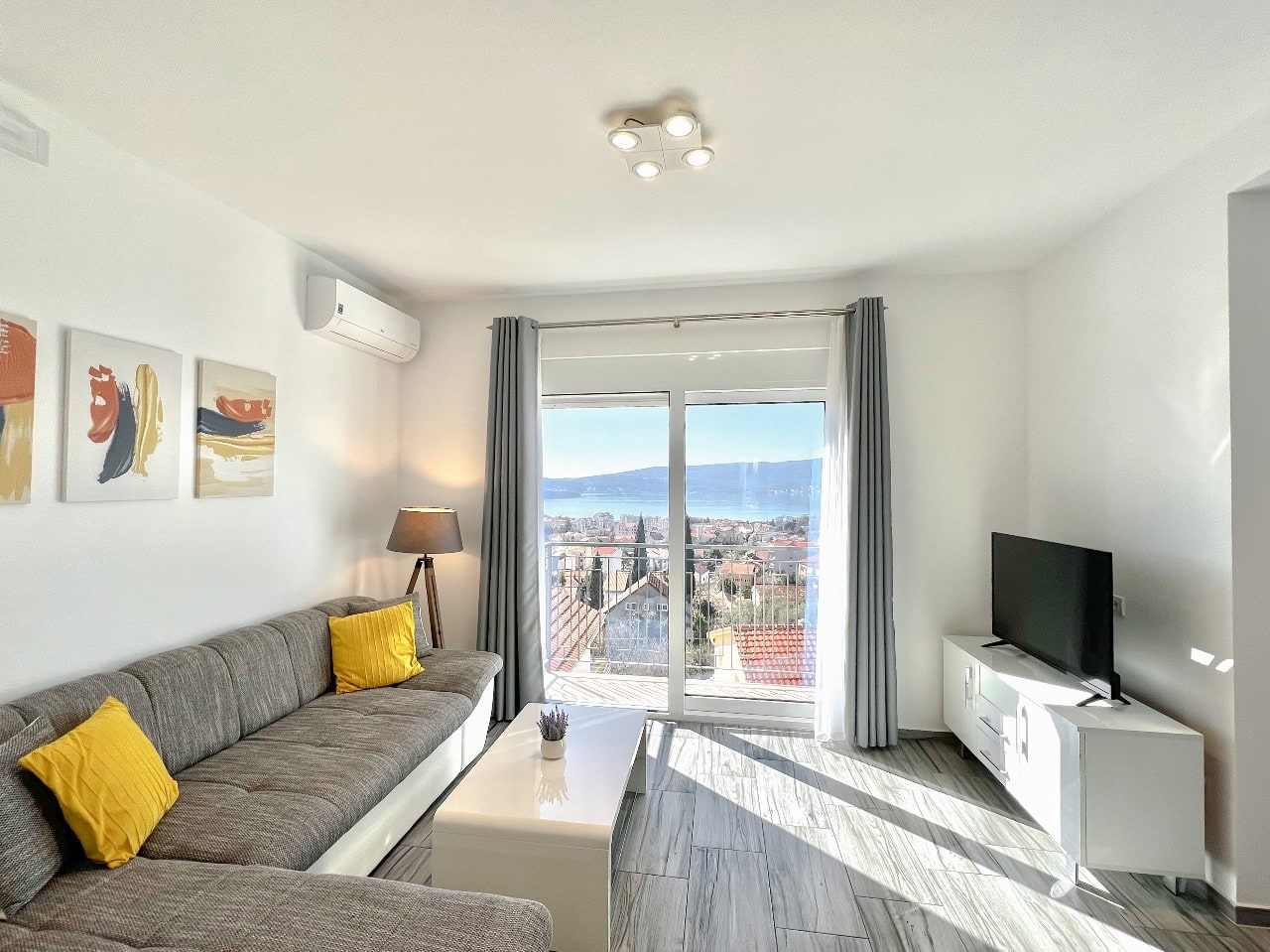 Bright living room in an apartment in Tivat, Montenegro: gray sofa, sea and mountain view, modern interior.