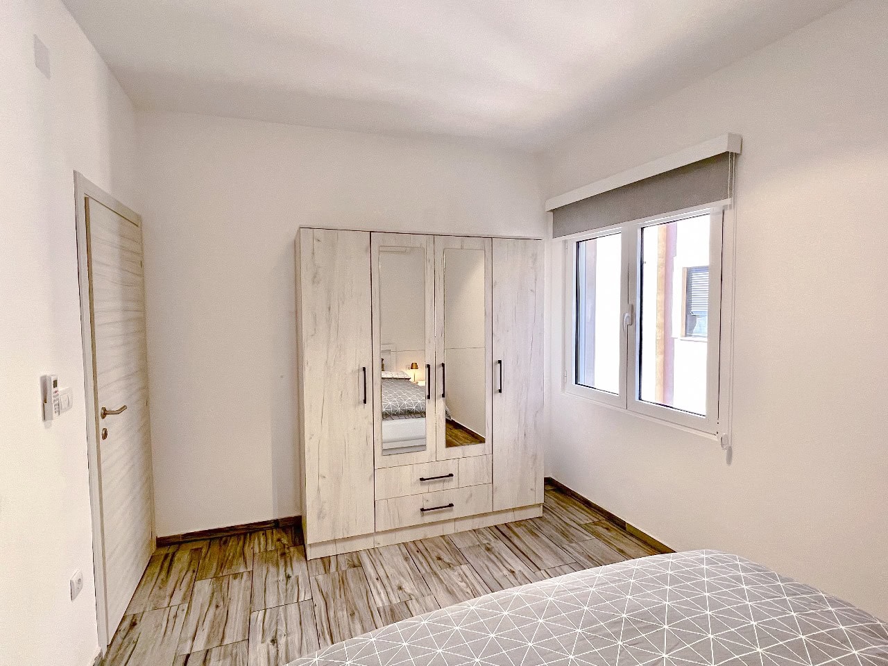 Bright bedroom in an apartment in Tivat, Montenegro: mirrored wardrobe, wood-look tile flooring, and modern interior.