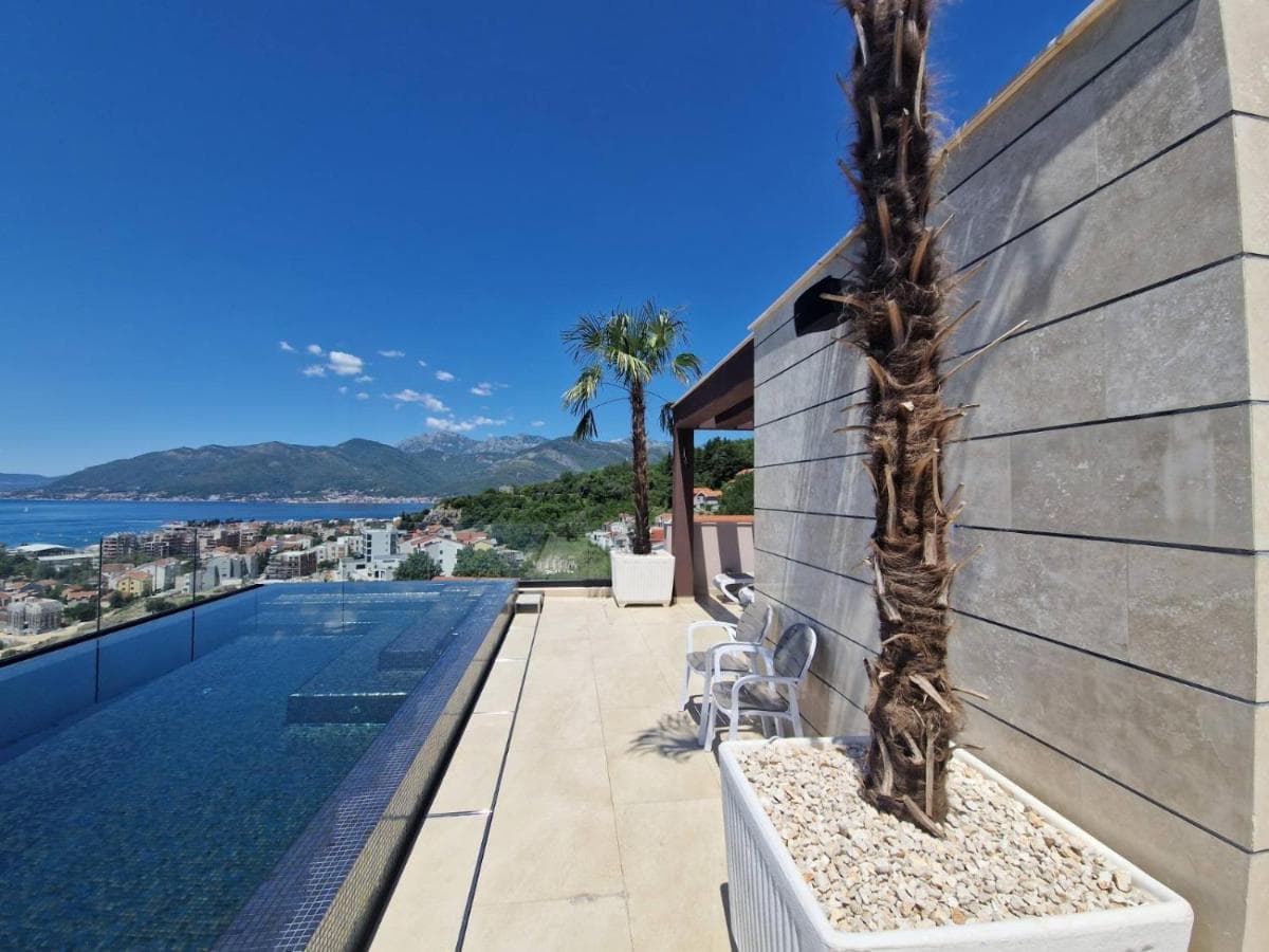 Terrace with an infinity pool and sea view in Tivat, Montenegro: modern stone finishes and palm trees.